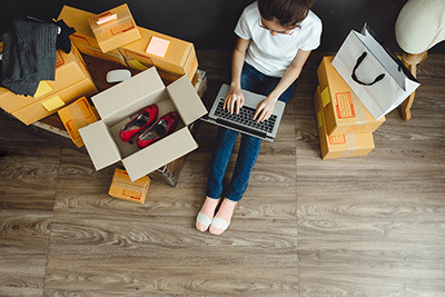 Woman with laptop sitting on floor with boxes scattered around.